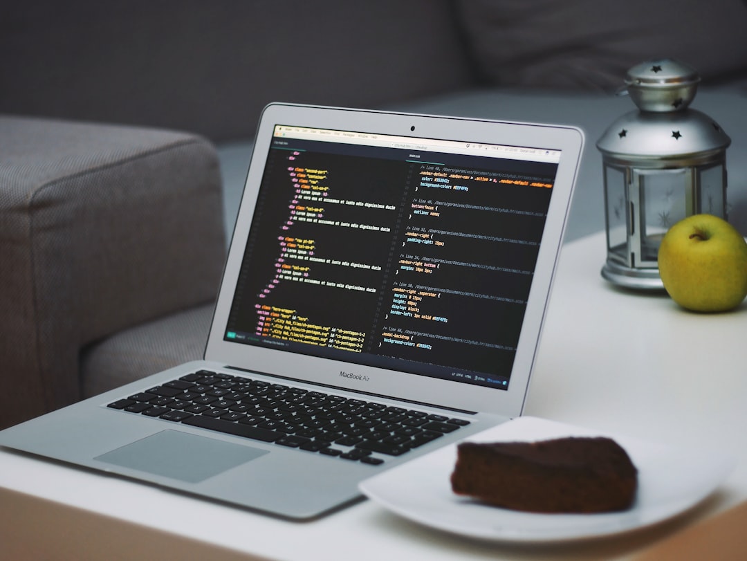 Laptop aberto em mesa de café mostrando código ao lado de bolo de chocolate na sala com sofá